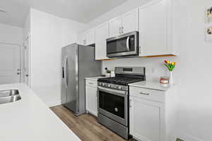 Kitchen with stainless steel appliances, wood finished floors, light countertops, white cabinetry, and baseboards