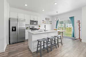 Kitchen with appliances with stainless steel finishes, a sink, wood finished floors, white cabinetry, and recessed lighting