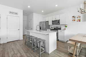 Kitchen with stainless steel appliances, a sink, wood finished floors, an island with sink, and a kitchen bar