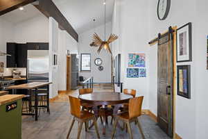 Dining space with high vaulted ceiling, baseboards, a barn door, and beamed ceiling