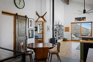 Dining room featuring high vaulted ceiling, ceiling fan, a barn door, wood finished floors, and a wood stove