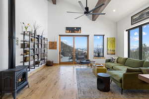 Living area with high vaulted ceiling, ceiling fan, light wood-style floors, a wood stove, and baseboards