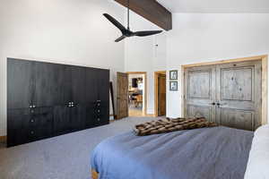 Carpeted bedroom with a high ceiling, beam ceiling, and ceiling fan