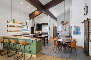 Kitchen with exhaust hood, a barn door, high vaulted ceiling, baseboards, and beam ceiling