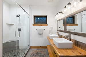 Bathroom featuring a stall shower, double vanity, and baseboards
