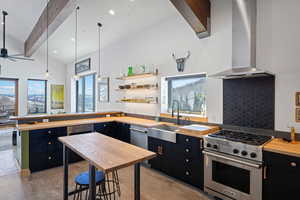 Kitchen with dark cabinets, luxury stove, butcher block countertops, a sink, and wall chimney range hood