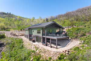 Rear view of house with a wooden deck, a forest view, board and batten siding, and solar panels