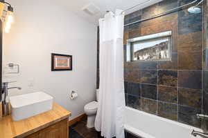 Bathroom featuring shower / bathtub combination with curtain, toilet, baseboards, and vanity