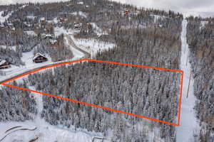 Snowy aerial view with property parcel outlined, a forest view, and a mountain view