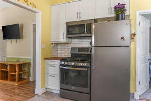 Kitchen with stainless steel appliances, white cabinetry, backsplash, and wood counters