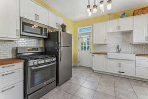 Kitchen with stainless steel appliances, wood counters, a sink, white cabinets, and decorative backsplash