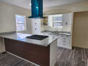 Kitchen featuring a sink, island exhaust hood, white cabinetry, stainless steel gas stovetop, and a peninsula