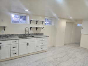 Kitchen with a sink, open shelves, light stone countertops, white cabinets, and baseboards