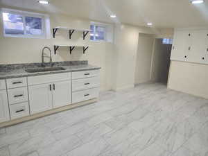 Kitchen with a sink, open shelves, light stone counters, white cabinetry, and recessed lighting