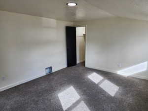 Carpeted empty room with a textured ceiling, baseboards, and vaulted ceiling