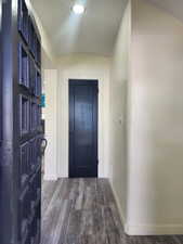 Doorway to outside featuring dark wood-style flooring, baseboards, and lofted ceiling