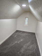 Bonus room featuring a textured ceiling, baseboards, carpet floors, and lofted ceiling