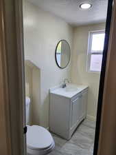 Half bath with a textured ceiling, toilet, vanity, and baseboards