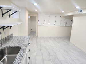 Interior space featuring a sink, white cabinets, light stone countertops, baseboards, and light marble finish floors
