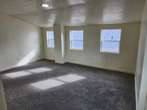 Spare room with a textured ceiling, baseboards, and dark colored carpet