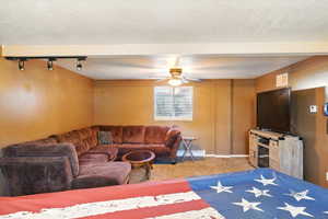 Carpeted living area featuring baseboard heating, a ceiling fan, baseboards, a textured ceiling, and rail lighting