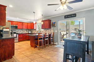 Kitchen with appliances with stainless steel finishes, reddish brown cabinets, dark countertops, backsplash, and ornamental molding