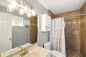 Full bathroom featuring tiled shower, toilet, vanity, and crown molding