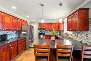 Kitchen with appliances with stainless steel finishes, a sink, dark brown cabinets, backsplash, and crown molding
