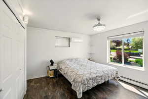 Bedroom featuring a baseboard radiator, crown molding, a wall unit AC, baseboards, and a closet