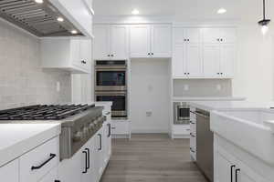 Kitchen featuring wall chimney range hood, appliances with stainless steel finishes, backsplash, white cabinetry, and recessed lighting