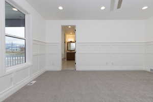 Empty room with a decorative wall, recessed lighting, light carpet, ceiling fan, and a wainscoted wall