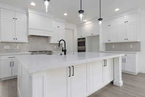 Kitchen with stainless steel double oven, tasteful backsplash, custom exhaust hood, light wood-style flooring, and white cabinetry