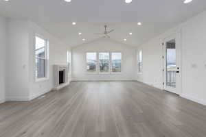 Unfurnished living room with ceiling fan, light wood-type flooring, lofted ceiling, a fireplace with raised hearth, and baseboards