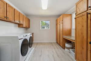 Laundry room with washing machine and dryer, cabinet space, light wood-style floors, baseboards, and ornamental molding
