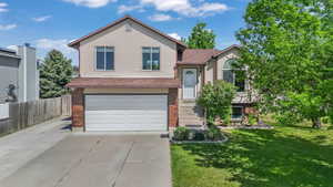 Tri-level home with brick siding, a garage, driveway, and a shingled roof
