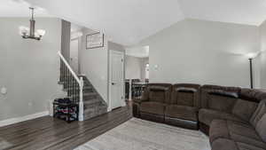 Living room featuring a chandelier, wood finished floors, stairway, vaulted ceiling, and baseboards