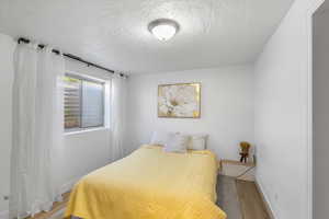Bedroom with wood finished floors, a textured ceiling, and baseboards