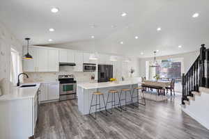 Kitchen with stainless steel appliances, a sink, under cabinet range hood, lofted ceiling, and a breakfast bar area