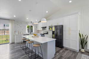 Kitchen with stainless steel appliances, a sink, a kitchen island, dark wood-type flooring, and lofted ceiling