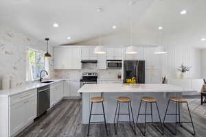 Kitchen featuring stainless steel appliances, a sink, a breakfast bar, vaulted ceiling, and white cabinets
