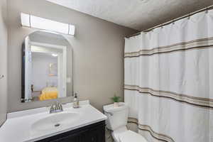 Full bath featuring vanity, toilet, a textured ceiling, and connected bathroom