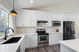Kitchen featuring appliances with stainless steel finishes, under cabinet range hood, a sink, lofted ceiling, and healthy amount of natural light