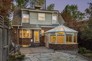 Back of property at dusk with a fenced backyard, brick siding, a patio, a shingled roof, and a sunroom