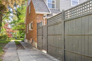 View of property exterior featuring brick siding, a shingled roof, and fence