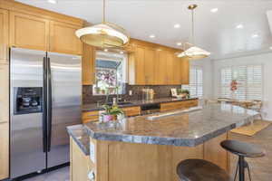 Kitchen with stainless steel fridge with ice dispenser, backsplash, dark countertops, recessed lighting, and a kitchen bar
