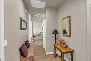 Hall with a chandelier, light wood-style flooring, and baseboards