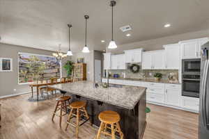 Kitchen with stainless steel appliances, white cabinets, decorative backsplash, a textured ceiling, and a breakfast bar area