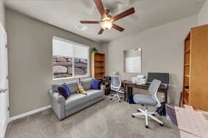 Carpeted home office featuring a ceiling fan and baseboards