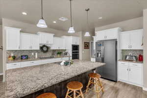 Kitchen with black appliances, a sink, light wood-type flooring, decorative backsplash, and white cabinetry