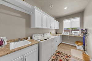 Clothes washing area featuring cabinet space, washer and dryer, light wood-style flooring, recessed lighting, and baseboards